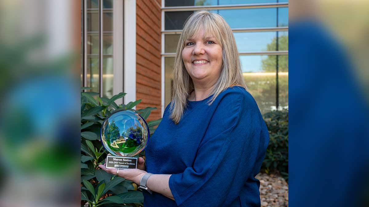 Person wearing blue shirt holds a green and blue glass award outside a building on the UT Institute of Agriculture campus.