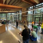 Several people hold clipboards and look at leaves on tables in the UT Arboretum Auditorium.